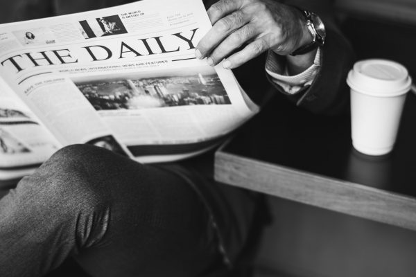 Business person reading a newspaper with coffee besides him